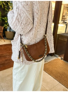 Close-up of brown suede bag with gold chain strap and ethnic beaded charm detail