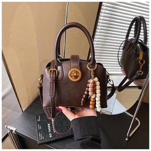 Nahaufnahme der braunen Shell-Tasche mit goldenem Drehverschluss und Perlenanhänger