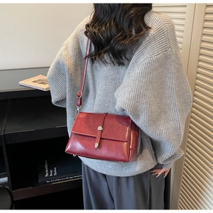 Detail of dark red crossbody bag with adjustable strap and metal buckle on female model