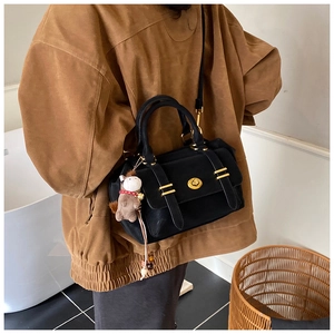 Detail of a matte black Boston bag with gold twist lock and a plush pony charm accessory