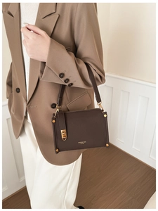 Close-up of brown pebbled leather shoulder bag featuring gold hardware and logo branding