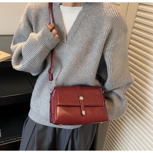Detail of dark red leather crossbody bag with silver buckle worn by a model