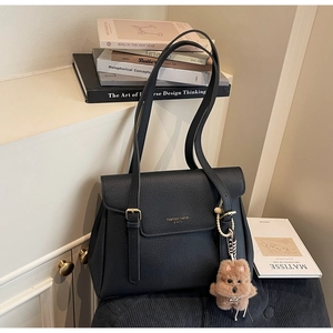 Détail d'un sac à rabat noir texturé litchi avec lettrage doré et charme d'ours peluche