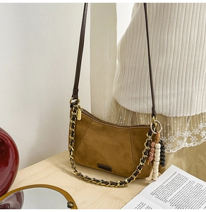 Detail of brown suede crossbody bag with gold chain strap and decorative beads