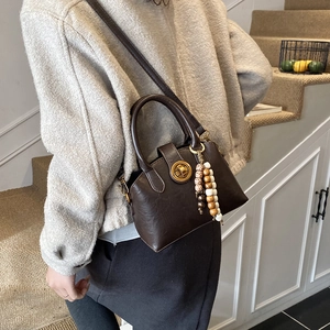 Detailansicht der braunen Leder-Muscheltasche mit Goldverschluss und Perlenanhänger