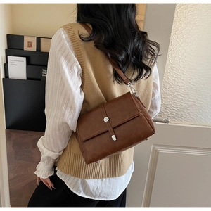 Close-up of a vintage brown crossbody bag featuring a silver buckle and textured leather