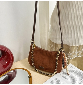 Detail of brown suede underarm bag with gold chain strap and wooden bead charm