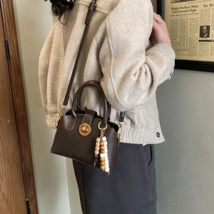Detail einer braunen Retro-Tasche mit goldenem Schloss und dekorativem Perlenanhänger