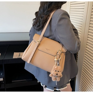 Detail of camel lychee leather tote bag with flap design and cute plush dog pendant