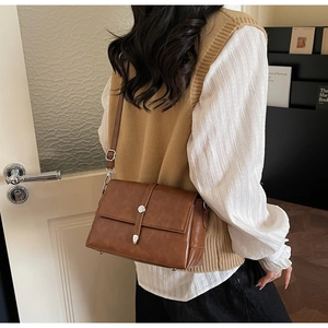 Close-up of a vintage brown crossbody bag with silver buckle on a textured faux leather