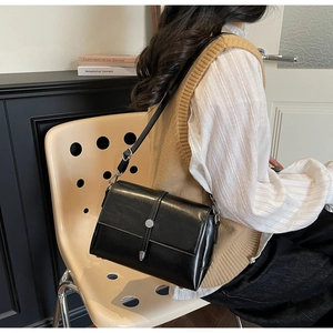 Chic black leather crossbody bag with silver buckle worn by model in minimalist interior