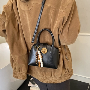 Schwarze Muschel-Tasche aus Leder mit goldenen Details und Perlenanhänger am Model