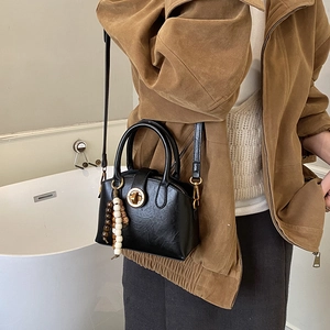 Detailansicht der schwarzen Muscheltasche mit goldenem Verschluss und Perlenanhänger