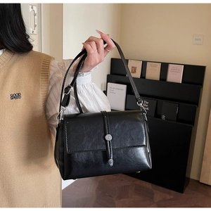 Close-up of black PU leather shoulder bag featuring silver hardware and flap closure