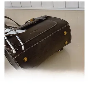 Detail of dark brown matte leather bag with white stitching and golden bottom studs