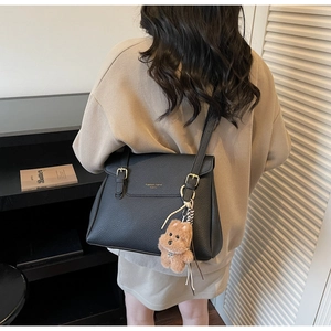 Détail du sac cabas en cuir grainé noir avec boucle dorée et breloque ours sur un modèle