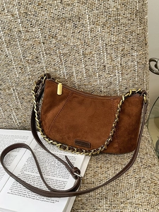 Vintage brown faux suede crossbody bag with gold chain strap on textured fabric