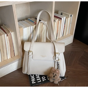 Détail du sac cabas crème avec texture litchi et pendentif ours sur une étagère