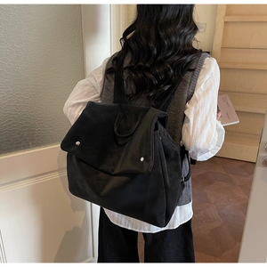 Rear view of model wearing black minimalist backpack with silver buckles in interior setting