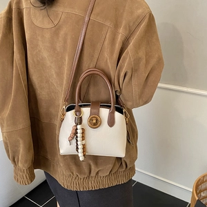 Detail einer beige-braunen Muschel-Tasche mit goldenem Drehverschluss und Perlenanhänger