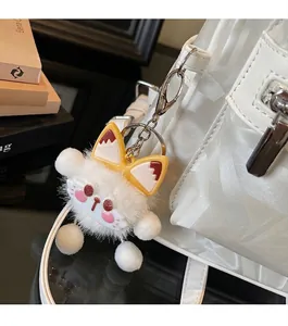 Close-up of white plush cat charm with yellow bow and metal ring on a backpack
