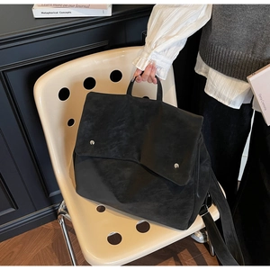 Detail of minimalist black matte leather handbag with silver buttons on a beige chair