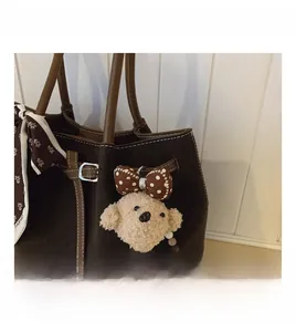 Close-up of brown suede tote bag featuring a floral silk scarf and plush bear charm detail