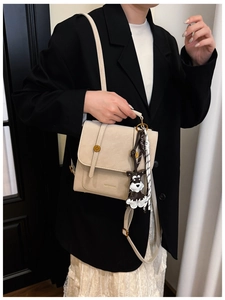 Detail of beige leather bag with metal knobs, schnauzer charm and woven shoulder strap