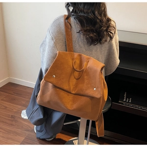 Close-up of warm brown suede backpack showing the flap cover and silver rivet details