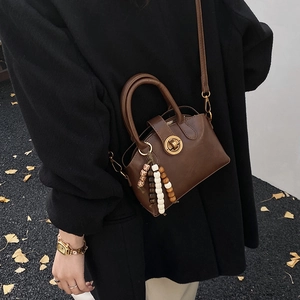 Detail einer braunen Schalentasche mit Vintage-Goldverschluss und buntem Perlenanhänger
