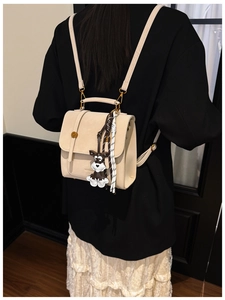 Detail of a beige mini backpack with a schnauzer charm on a model in a black suit