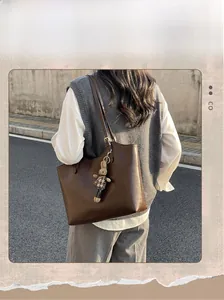 Detail view of large dark brown leather tote bag with a cute plaid bunny keychain charm