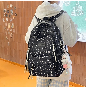 Detalle de mochila negra con estampado de estrellas y colgante de oso peluche