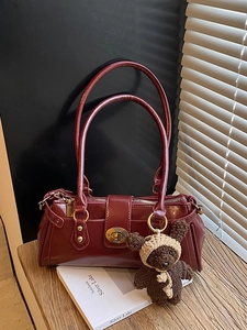 Retro burgundy leather pillow bag with gold clasp and brown knit bear charm on table