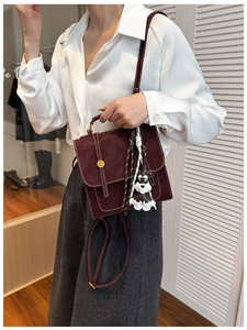 Detail of burgundy vintage crossbody bag with white stitching and puppy charm on model