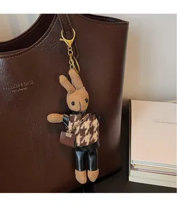 Close-up of a brown knitted rabbit keychain with houndstooth sweater on a leather tote bag