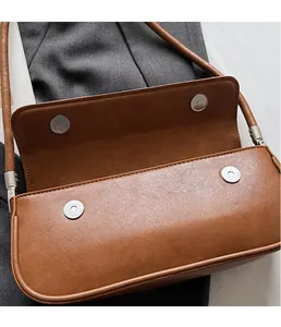 Detail of brown leather underarm bag featuring dual magnetic metal buckles and smooth texture