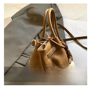 Detail of brown leather bucket bag showing metal hook and woven tassel accessory