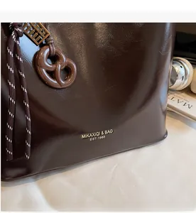 Detail of dark brown oil-wax leather tote with brand logo and vintage abacus charm