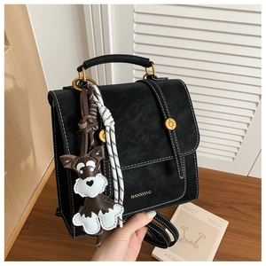Detail of black faux leather bag featuring white contrast stitching and a dog-shaped charm