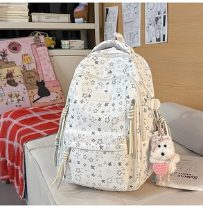 Detalle de mochila blanca con estampado de estrellas, bolsillo frontal y colgante de perro