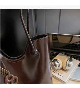 Detail of dark brown glossy leather tote bag with unique pretzel charm and round handle