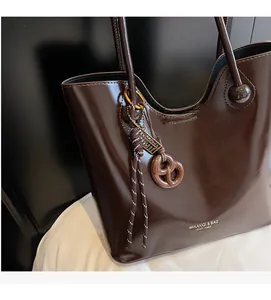Detailed close-up of dark brown glossy tote bag with braided knot and logo charm