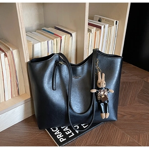 Detail of black faux leather tote bag with gold logo and stylish rabbit charm accessory