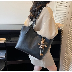 Detail of black leather tote bag with a minimalist print and a trendy rabbit doll charm