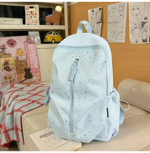 Detail view of light blue backpack with silver star patterns and multiple zipper pockets