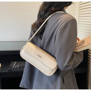 Detail of cream baguette bag with minimalist metal logo and sleek leather shoulder strap