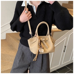 Detail view of beige bucket bag with tassel and adjustable strap on a model