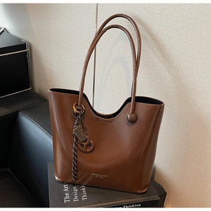 Detail view of brown glossy tote bag on a design book featuring gear charm and knot detail