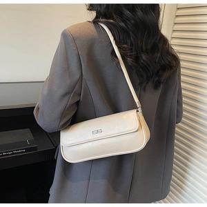 Detail of minimalist beige baguette shoulder bag with metallic logo on textured leather